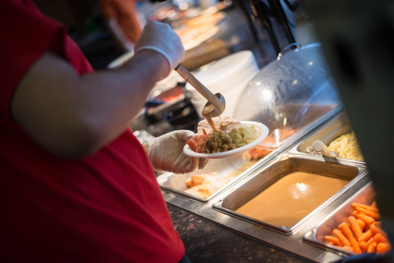 A worker pours gravy over a plate of turkey, mashed potatoes, carrots and stuffing