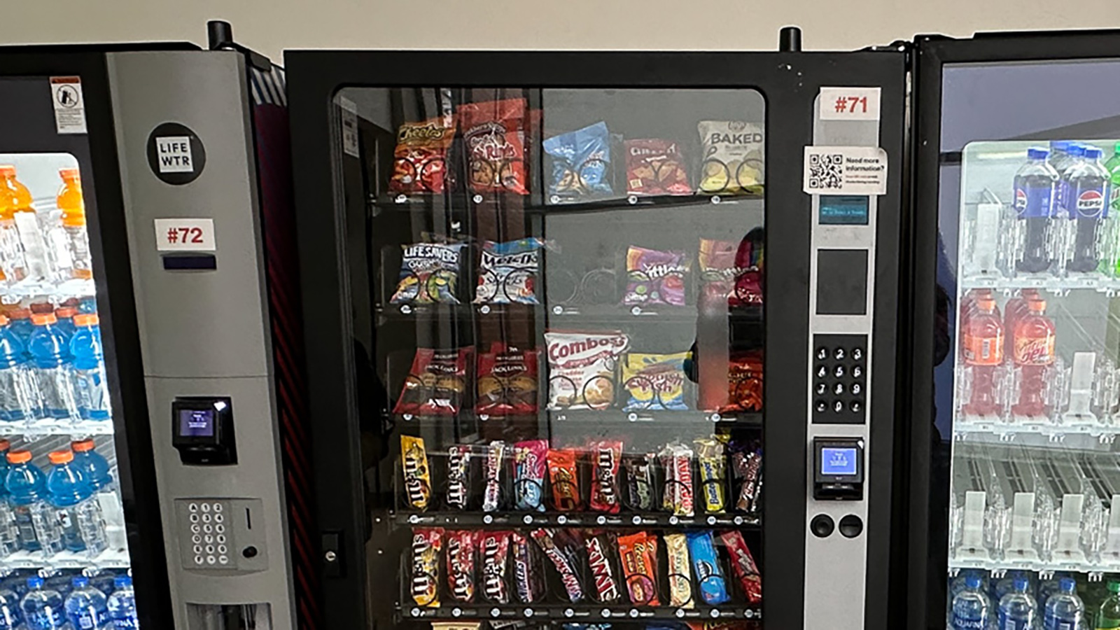 a row of vending machines stocked with various snacks and beverages, located in a well-lit area on campus.