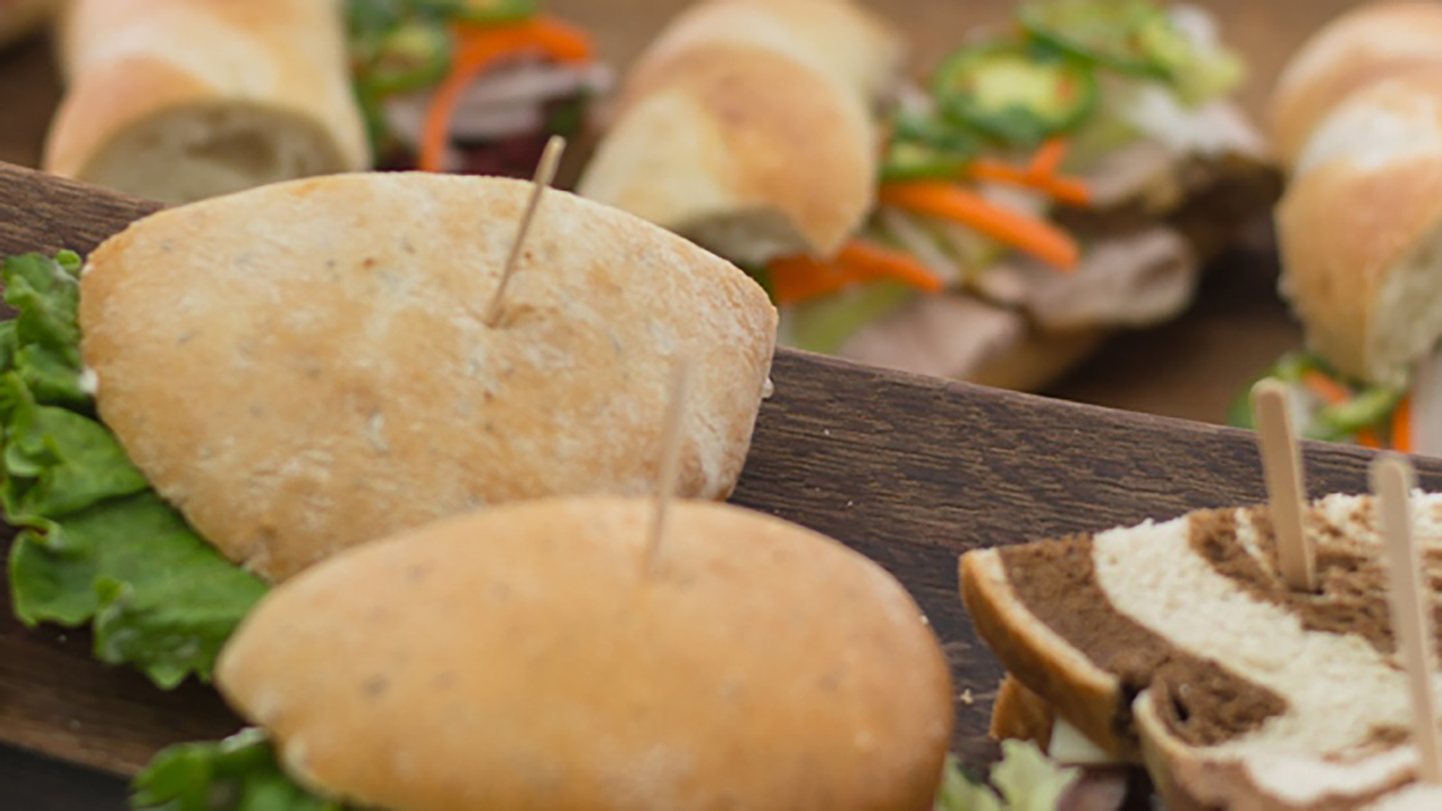 Lots of sandwiches and subs on a dark wooden board.