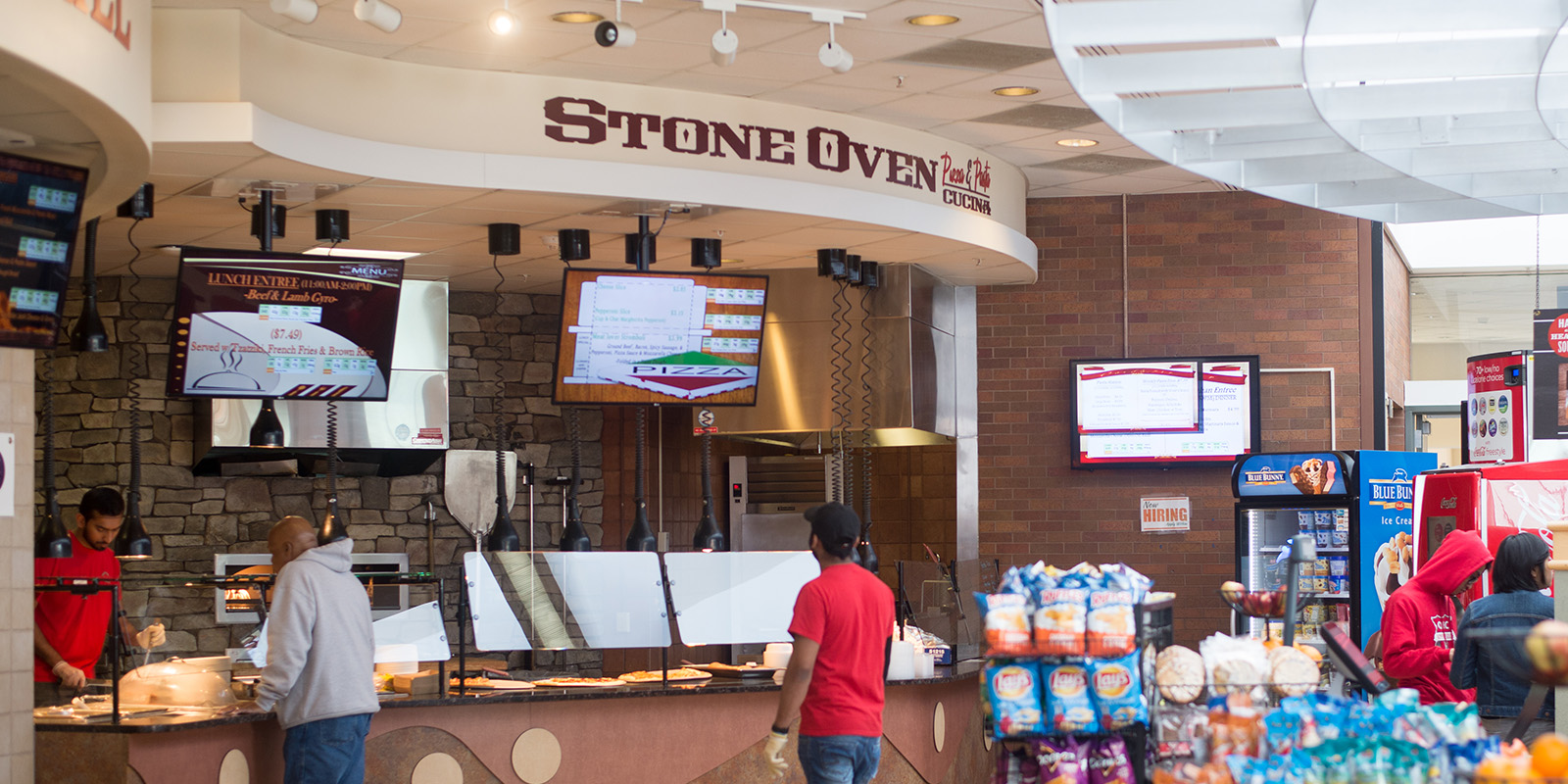 ﻿Interior of The Commons dining location with staff, digital menus, and a stone wall design.