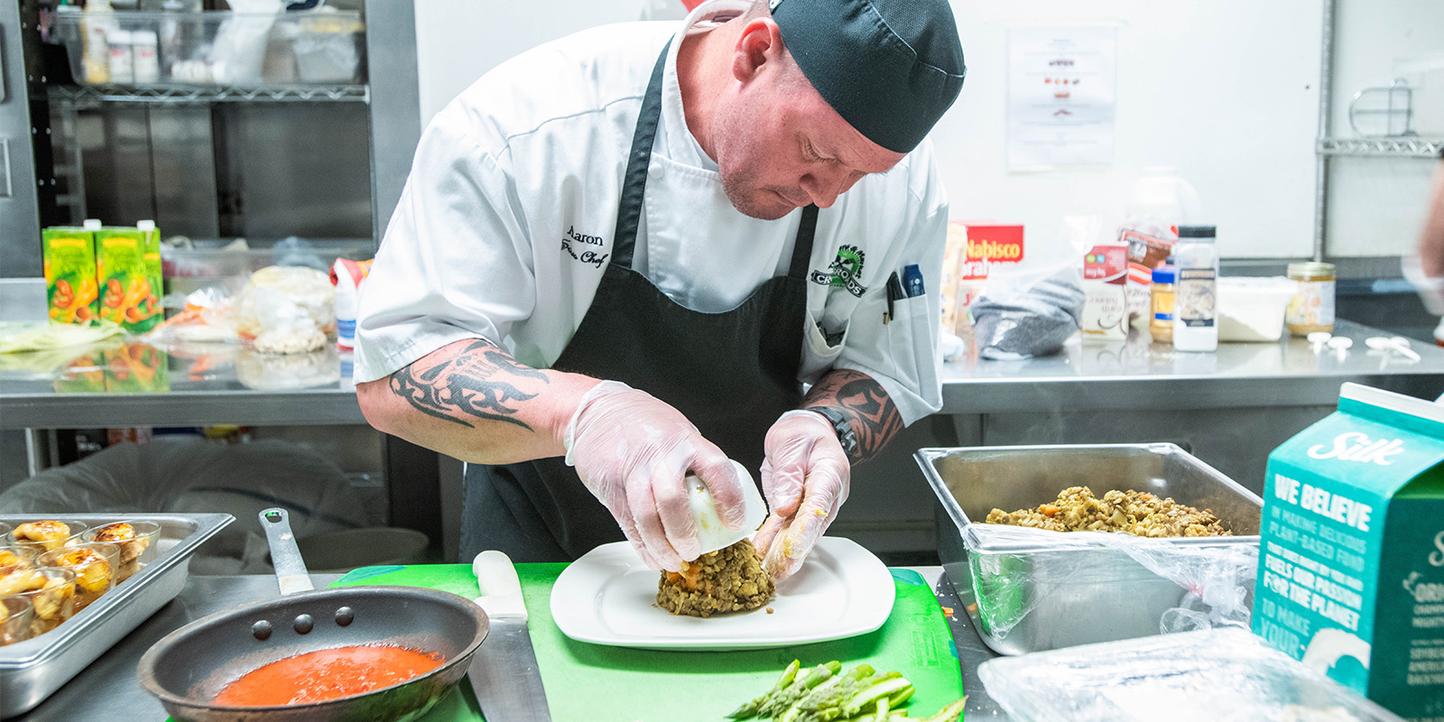 ﻿Chef in the kitchen plating food next to a pan of sauce