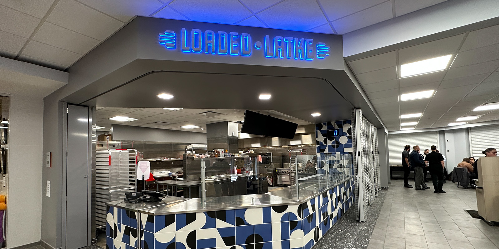 ﻿A modern food counter with a blue neon 'Loaded Latke' sign and tiled decor.