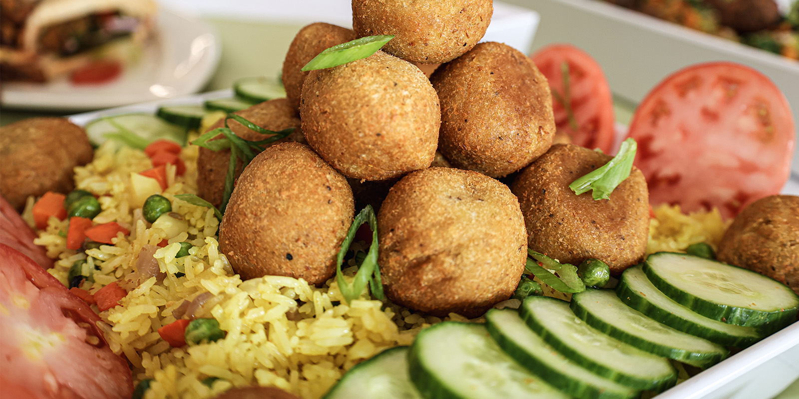 ﻿A plate of fried rice, cucumber, tomato and lentil balls