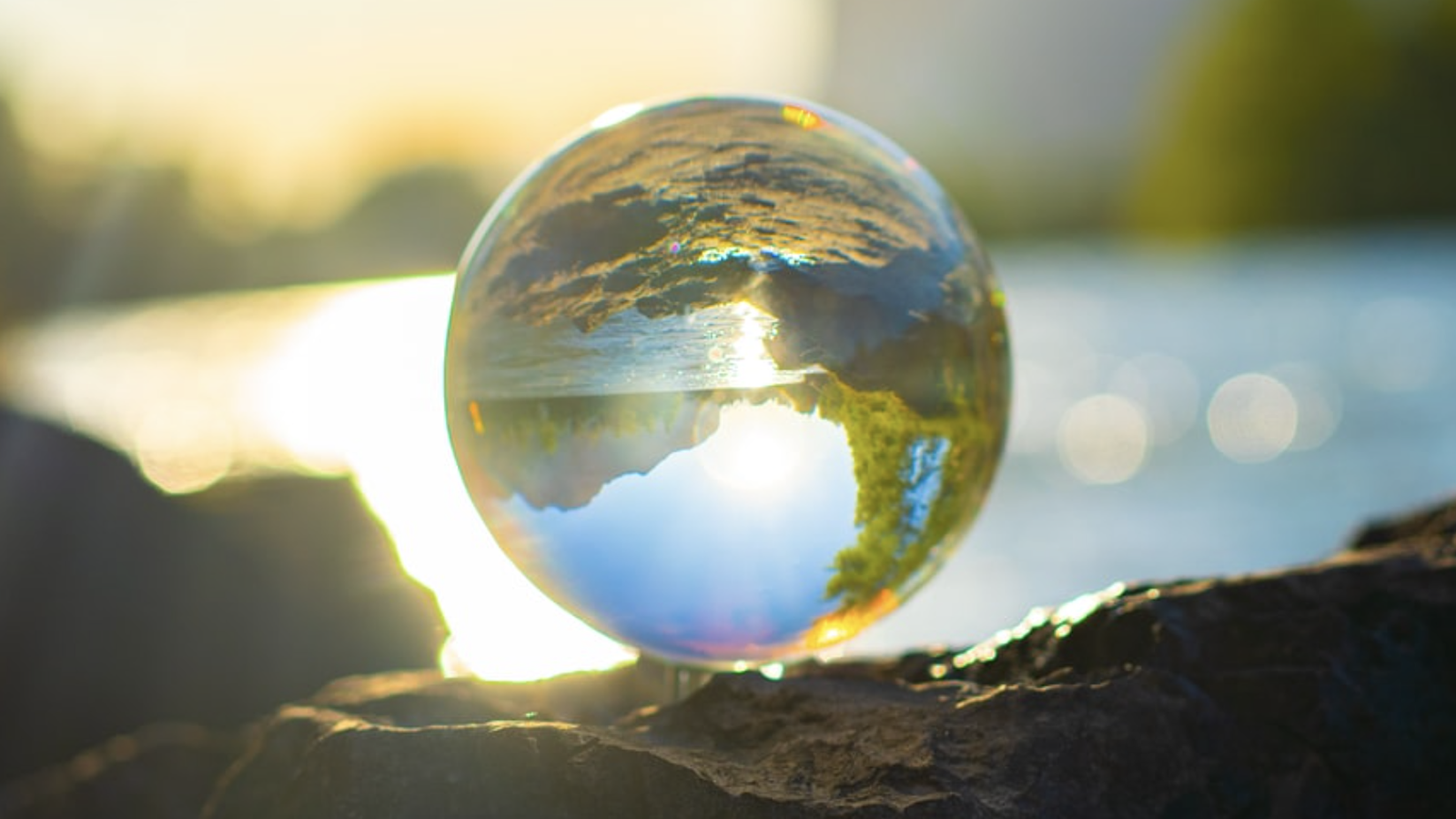 A crystal ball resting on a rocky surface with sunlight shining through it, creating an inverted refraction of the surrounding landscape and sky within the sphere.