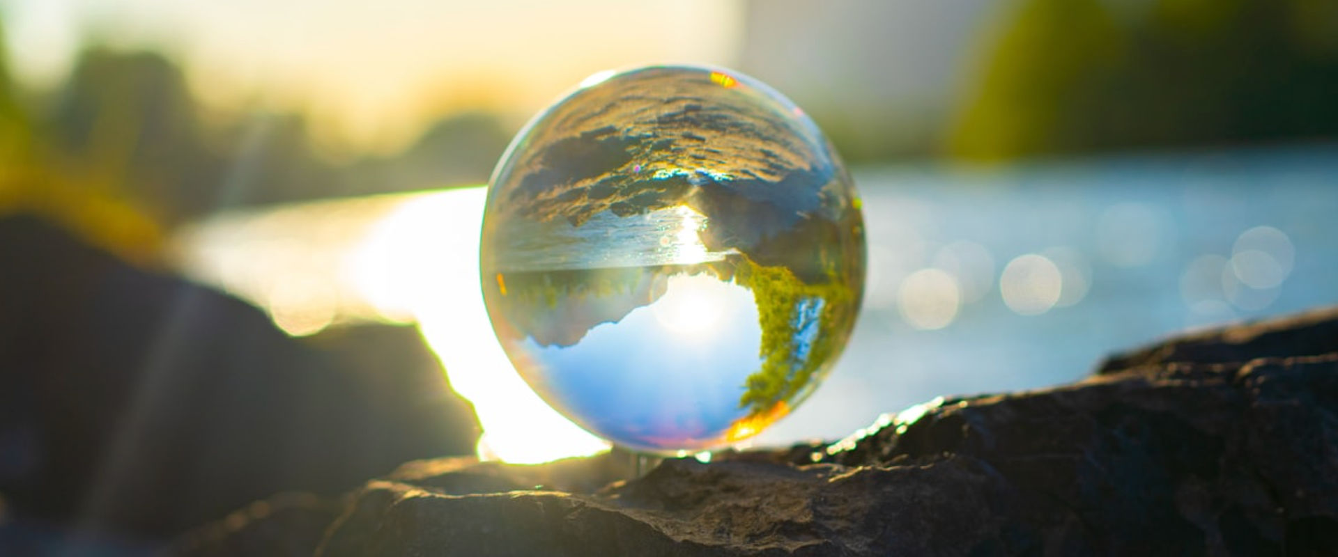 A crystal ball resting on a rocky surface with sunlight shining through it, creating an inverted refraction of the surrounding landscape and sky within the sphere.