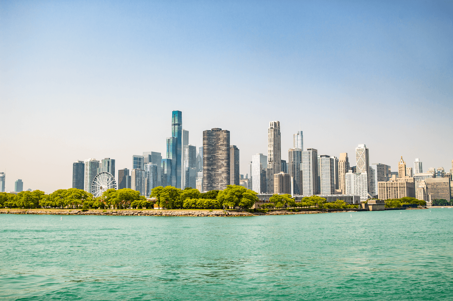 The image showcases a scenic view of Chicago's skyline from Lake Michigan. The foreground features the vibrant greenery of a lakeside park, while the background is dominated by a bustling cityscape with iconic high-rise buildings and skyscrapers.