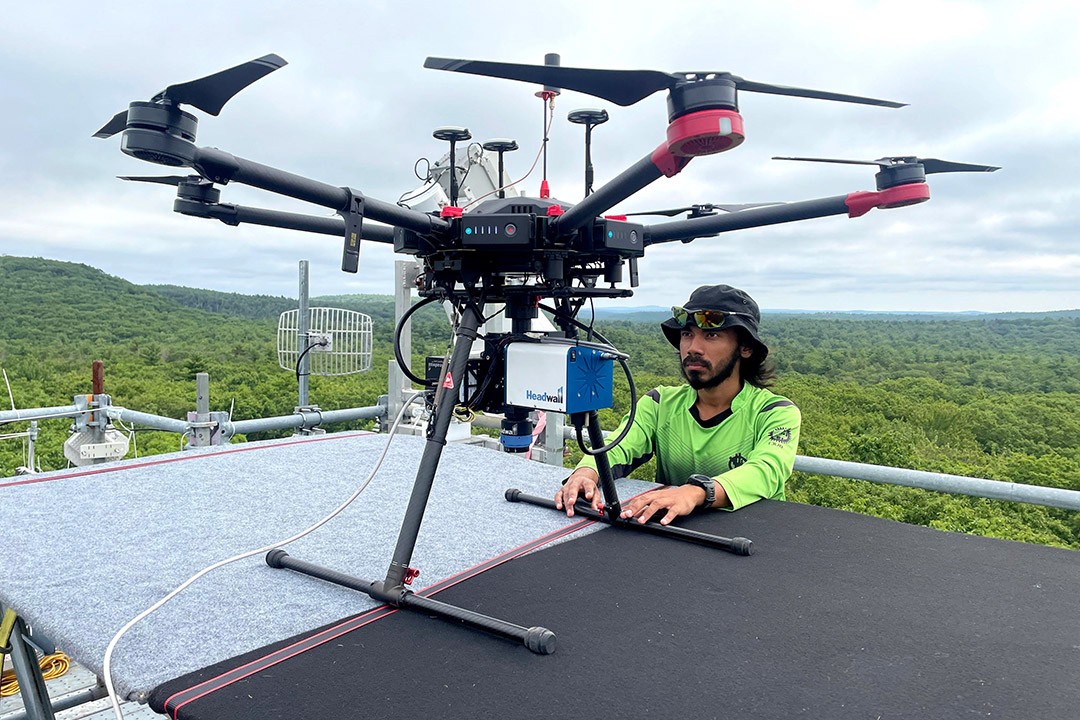 Man in neon green shirt and black cap operating a large drone with multiple rotors on a rooftop.