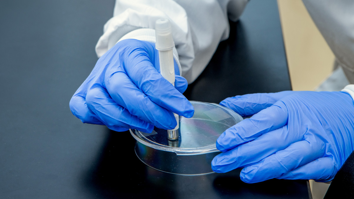 A pair of gloved hands works with a pen-like device.