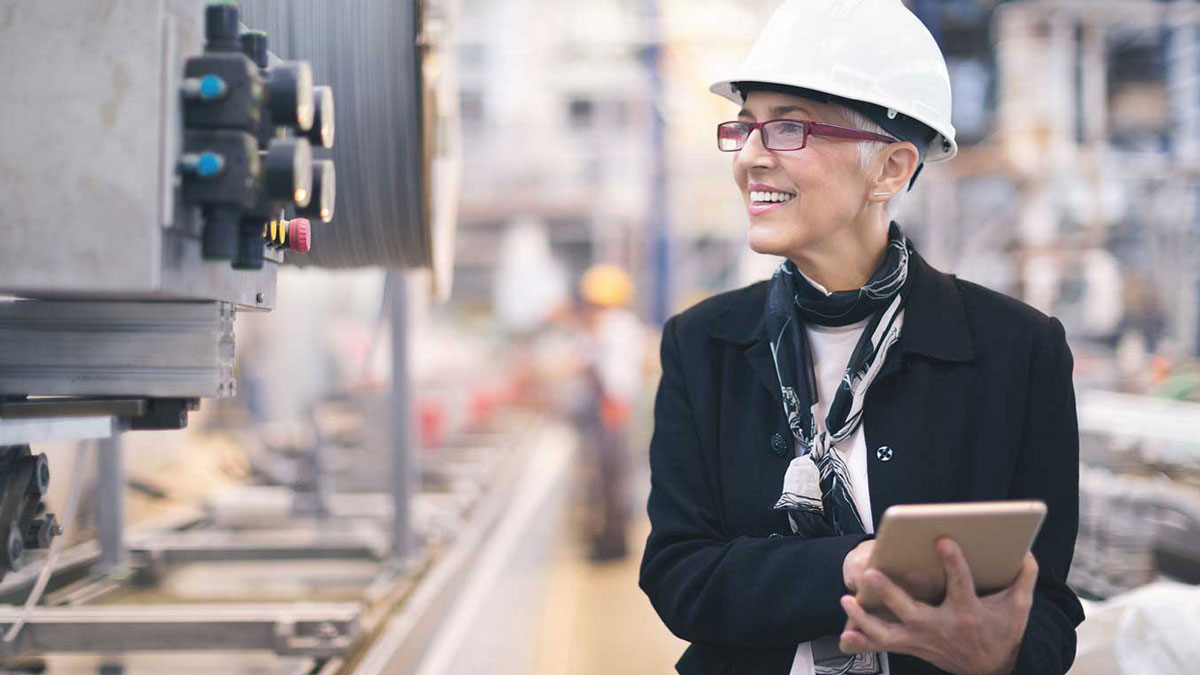 A women wearing a hard hat and glasses inspects a piece of equipment.