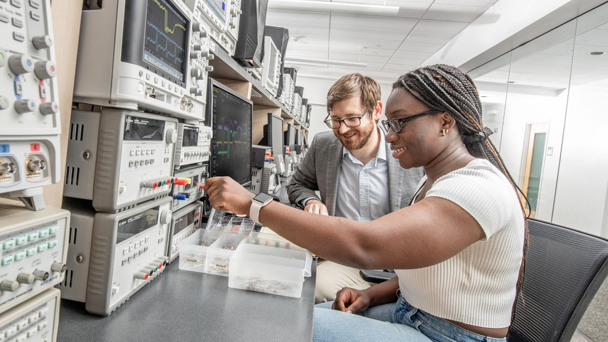 Student and professor work in front of electrical devices with various colored knobs.