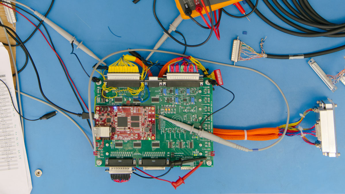 Circuit board on blue table surrounded by cords and papers.