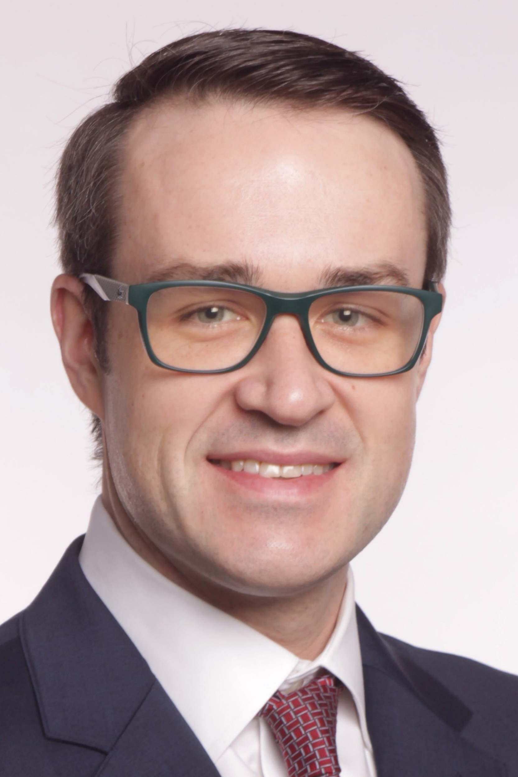 A headshot of Steve Skelley wearing a suit, tie, and green glasses.