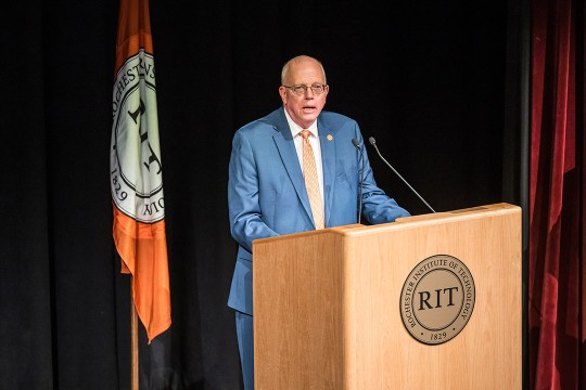 RIT President David Munson stands in front of a podium with the RIT seal on stage.