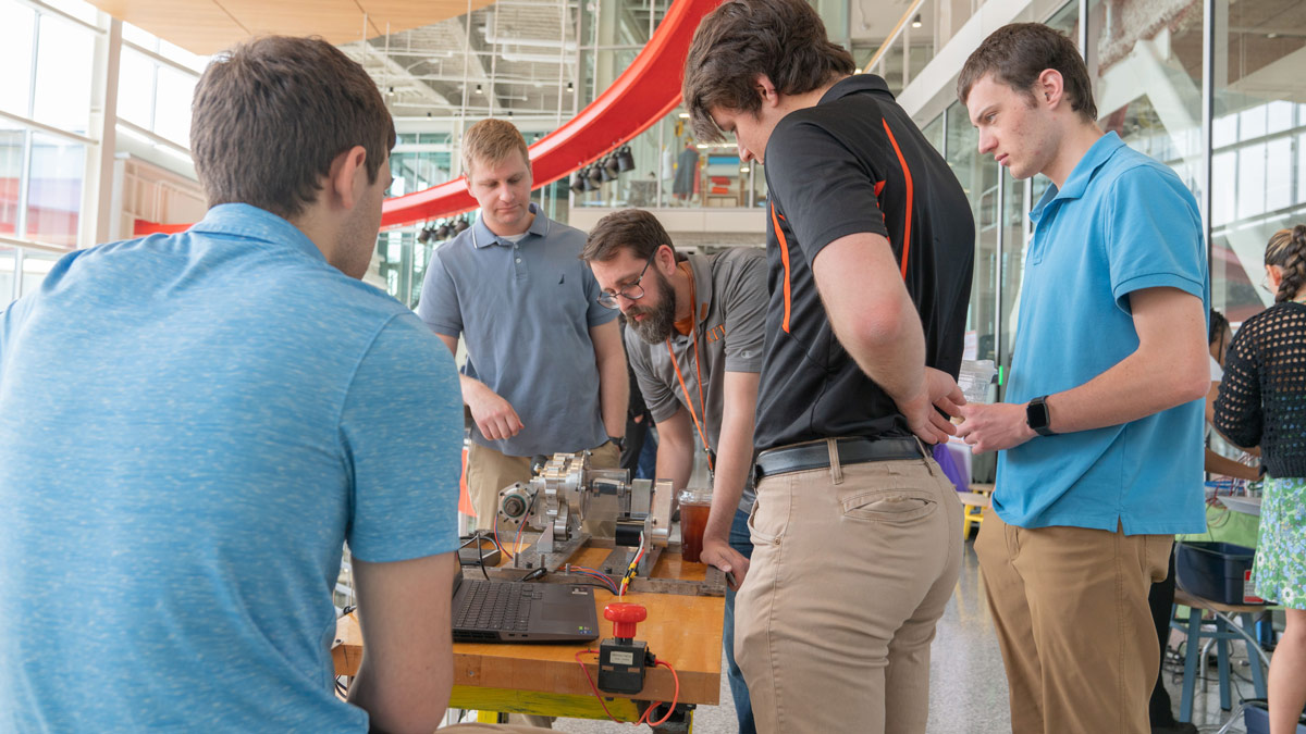 Students and professor stand around a mechanical device and a laptop.