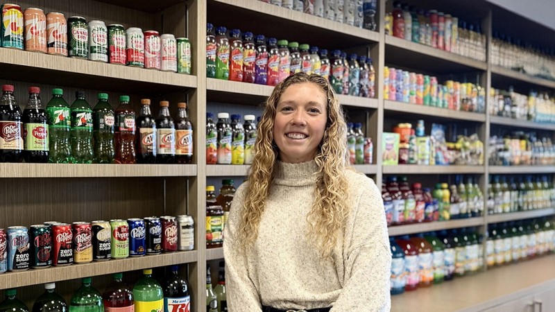 Anna Valentine, a packaging science graduate, stands in fornt of a display featuring products from Keurig Dr Pepper, inclduing bottles of Canada Dry, Squirt, and A&W soft drinks.
