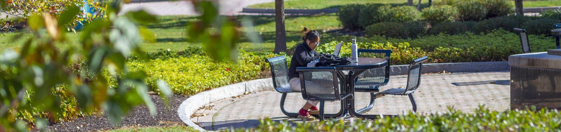A student sitting at a table outside during the summer.