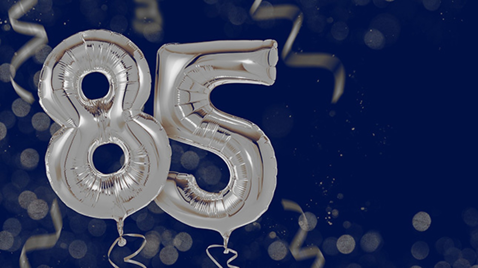 dark blue background with silver party balloons that form the number 85