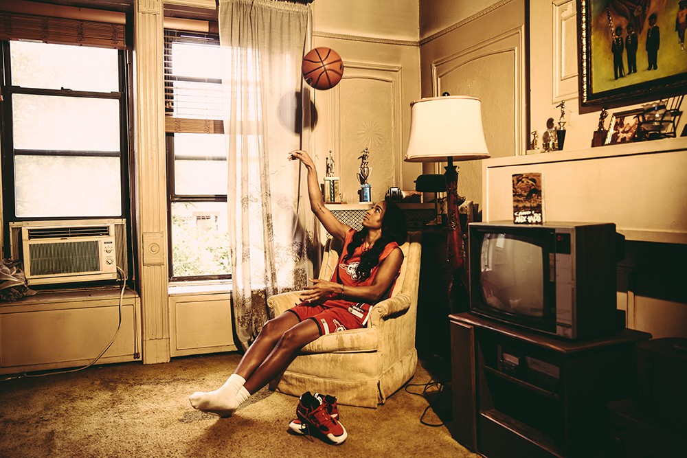 A person sitting in a living room chair throws a basketball in the air.