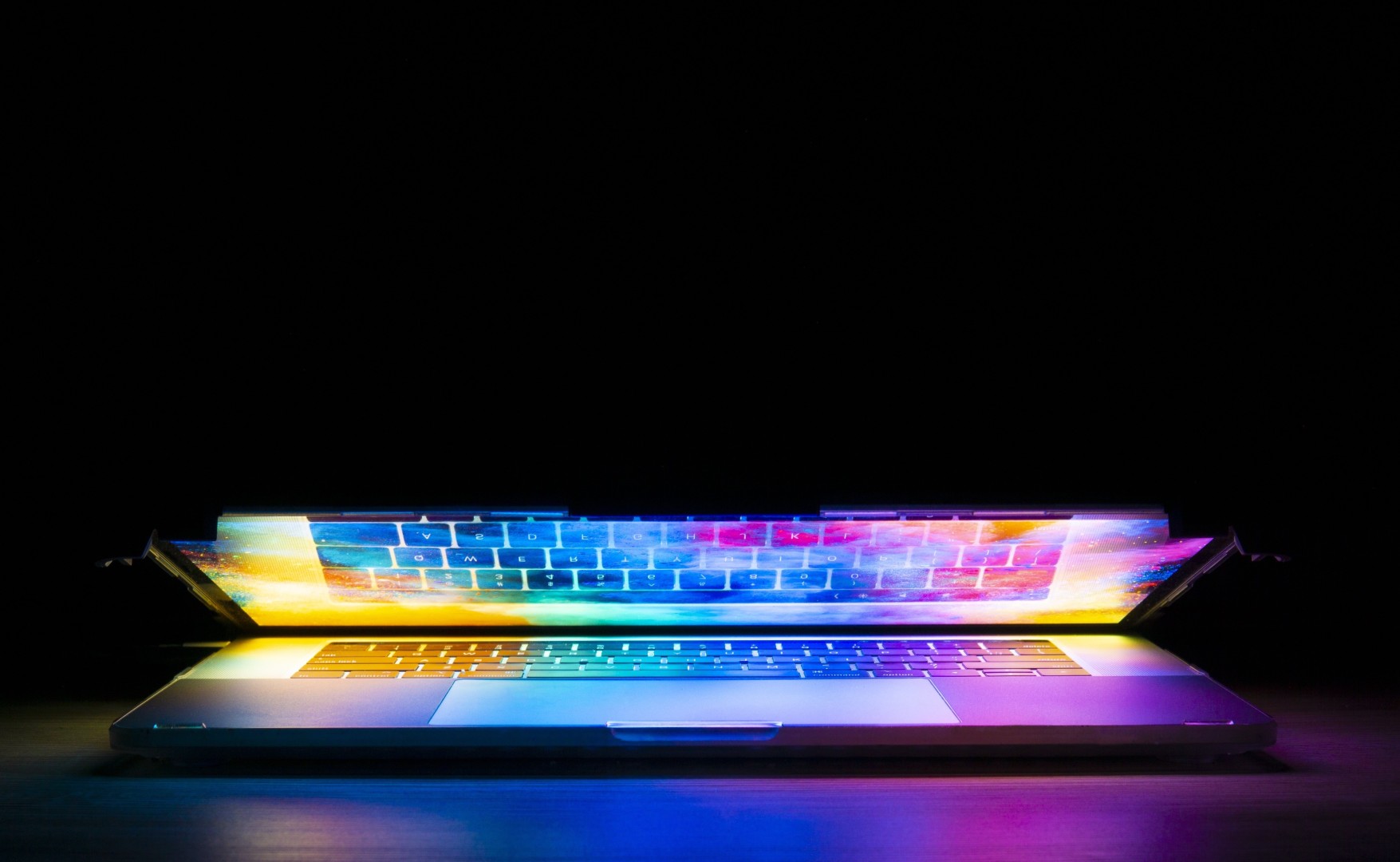 partially closed laptop computer with screen illuminating keyboard