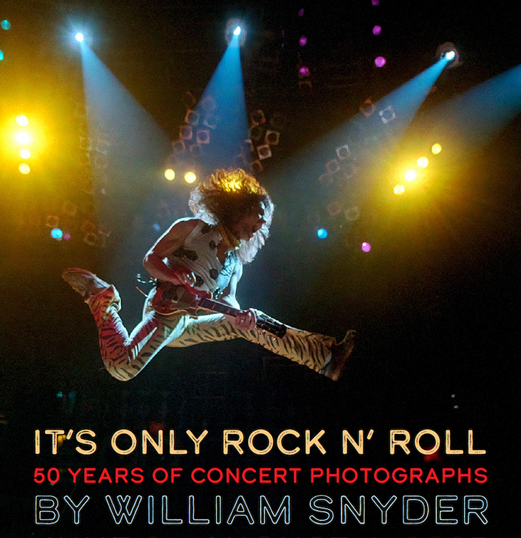 color photograph of a guitar playing musician leaping high on a performance stage.