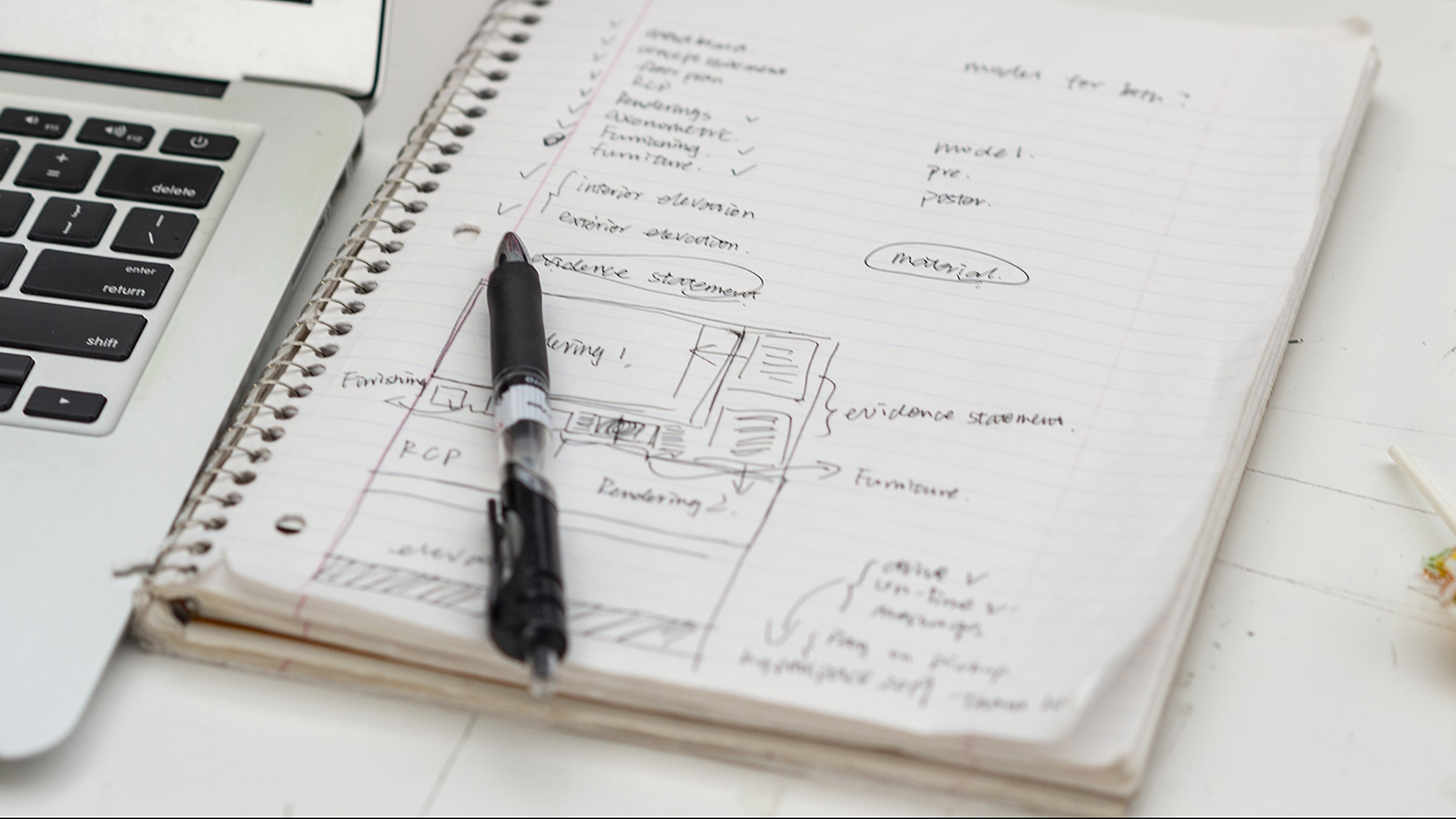 A notebook with handwritten notes and diagrams related to finance and accounting next to a laptop on a white desk.