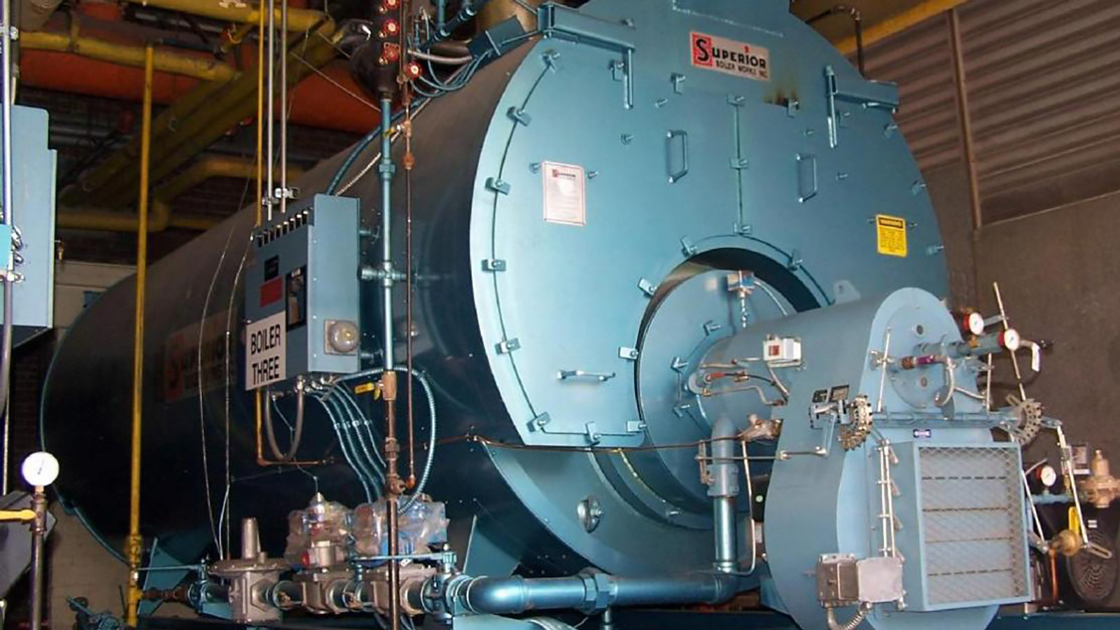 A large blue boiler in a room with concrete walls