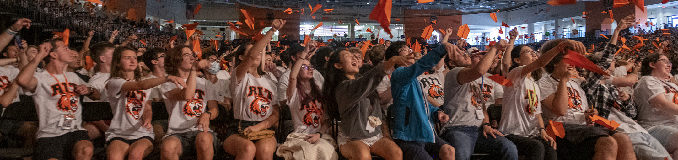 a row of students launching orange paper airplanes into the air