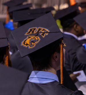 RIT's Class of 2024 processing in for the Commencement Ceremony. Photo is zoomed in on some graduation caps, one features the RIT Logo and mascot (Tiger)