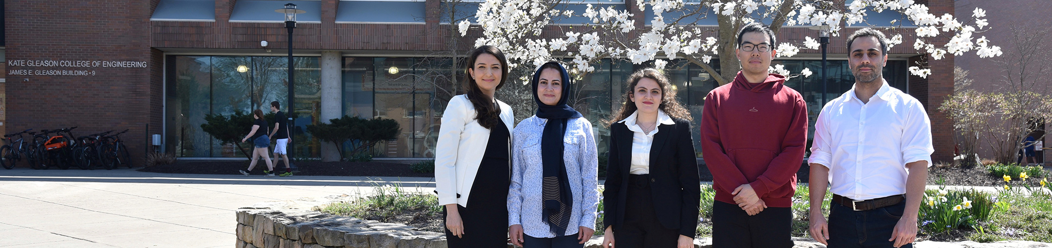 5 people standing outside, in front of a flowering tree.