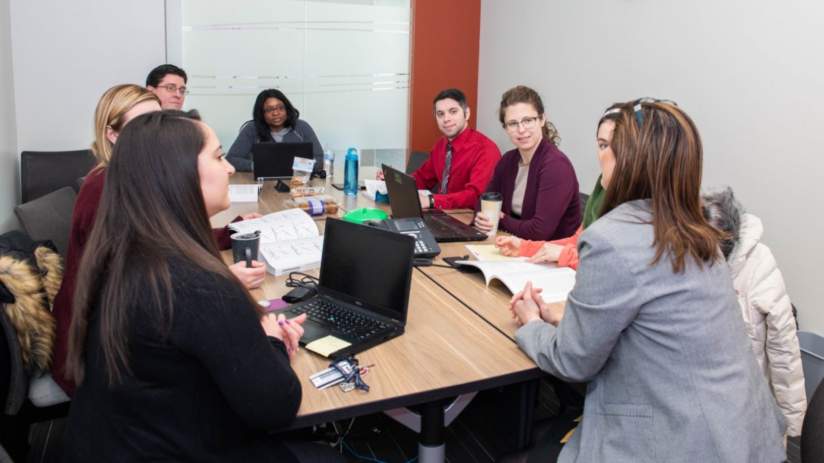 A diverse group of professionals collaborating in a conference room with laptops and books on the table.