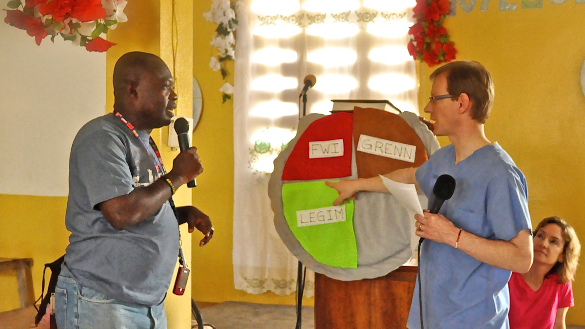 Two people talking on microphones in front of a pie chart written in a different language.