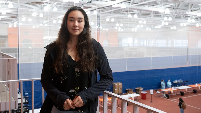 A female stduent stands along a railing in the RIT Field House, where COVID-19 testing takes place.