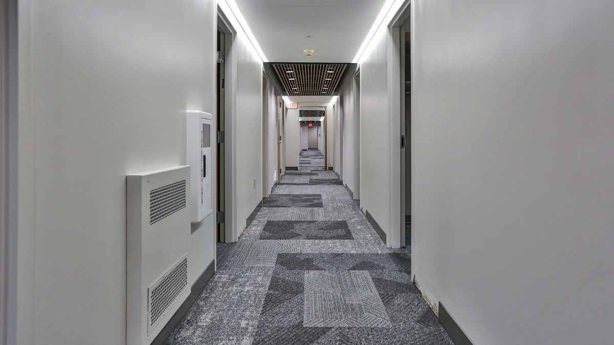 A long, carpeted residence hall hallway featuring pristine white walls, creating a clean and inviting atmosphere. 