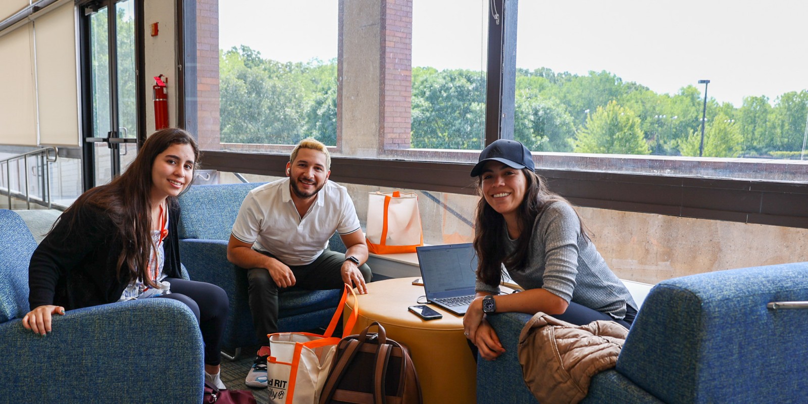 ﻿Three students sitting on comfy couch seats with a larger window behind them