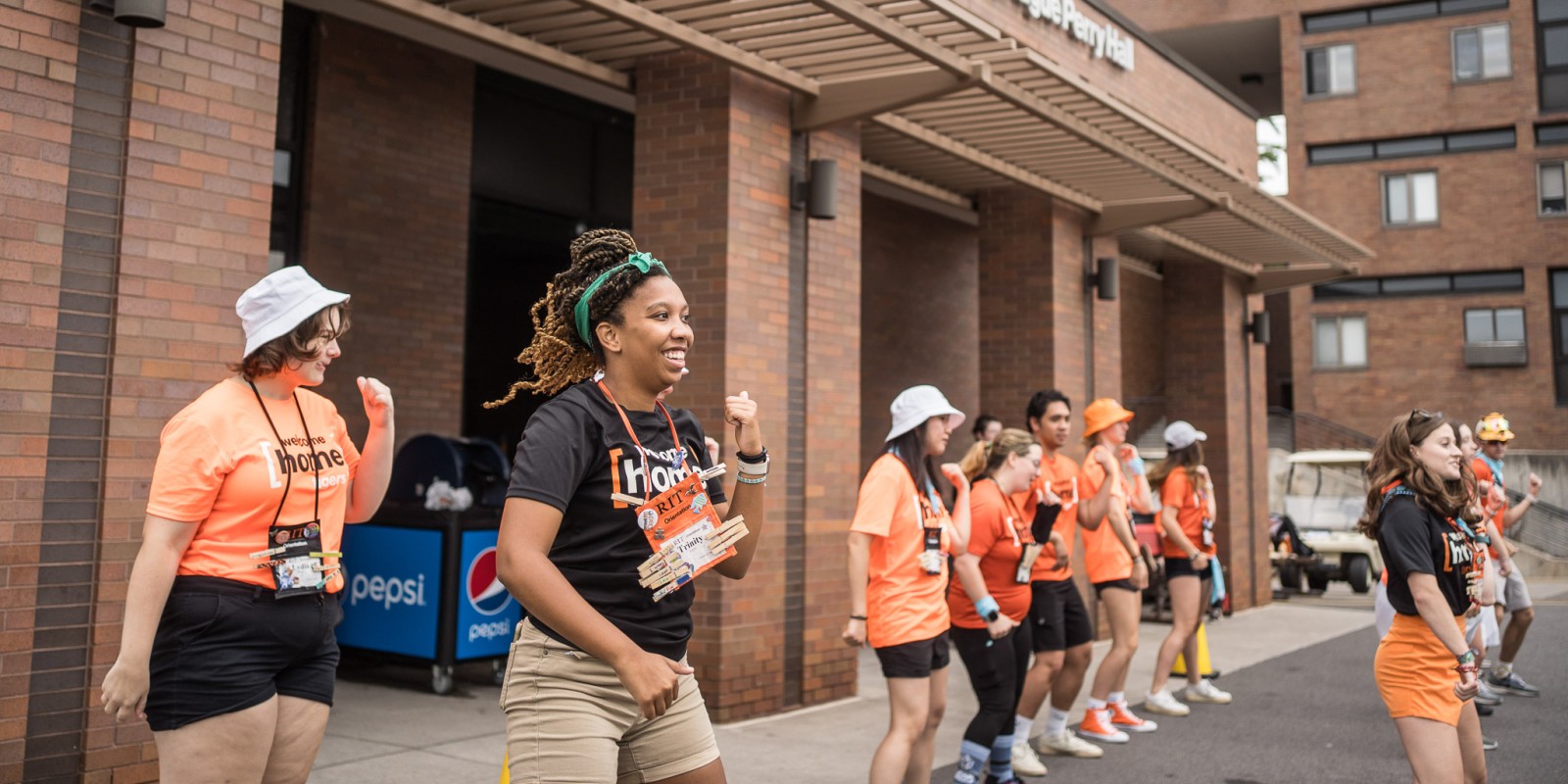 ﻿Student orientation workers outside of the residence hall dancing in a line with orange and black shirts that say welcome home tigers