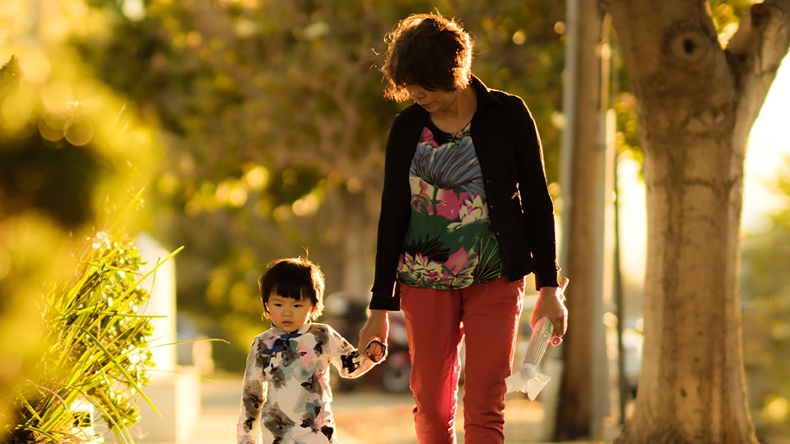 woman walking a child in a tree-lined neighborhood