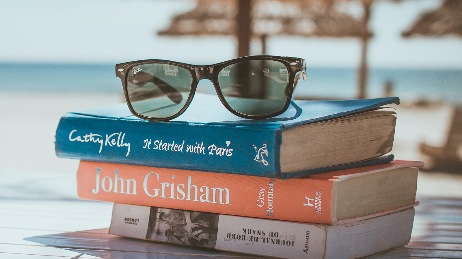 a beach scene featuring sunglasses atop a stack of books in the foreground