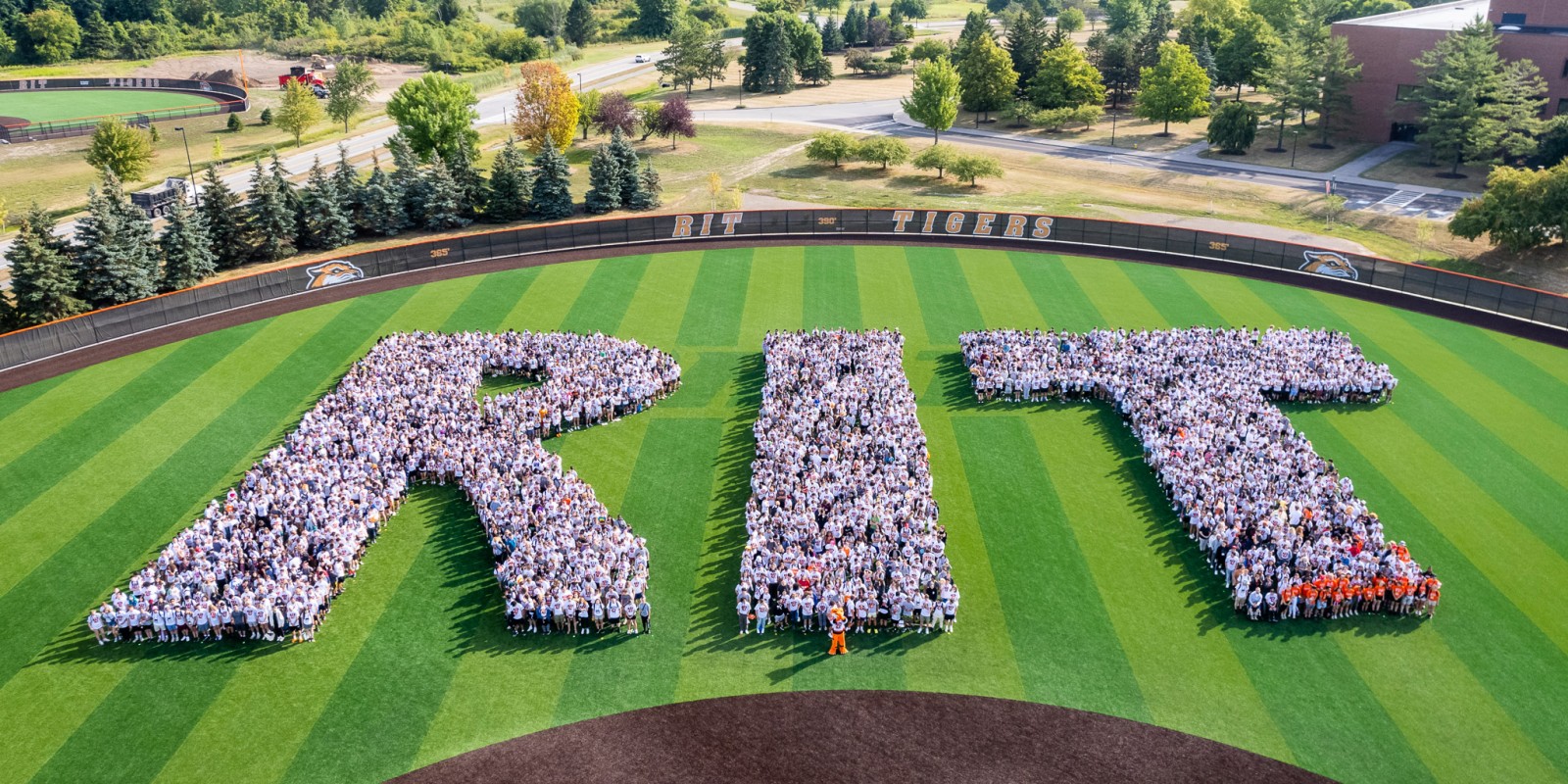 ﻿Overhead view of people in white shirts standing in the formation of the letter R I T outside on a turf field