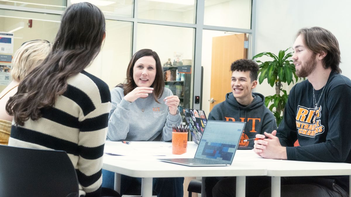 Students sit around a table with a coffee and laptop on it.