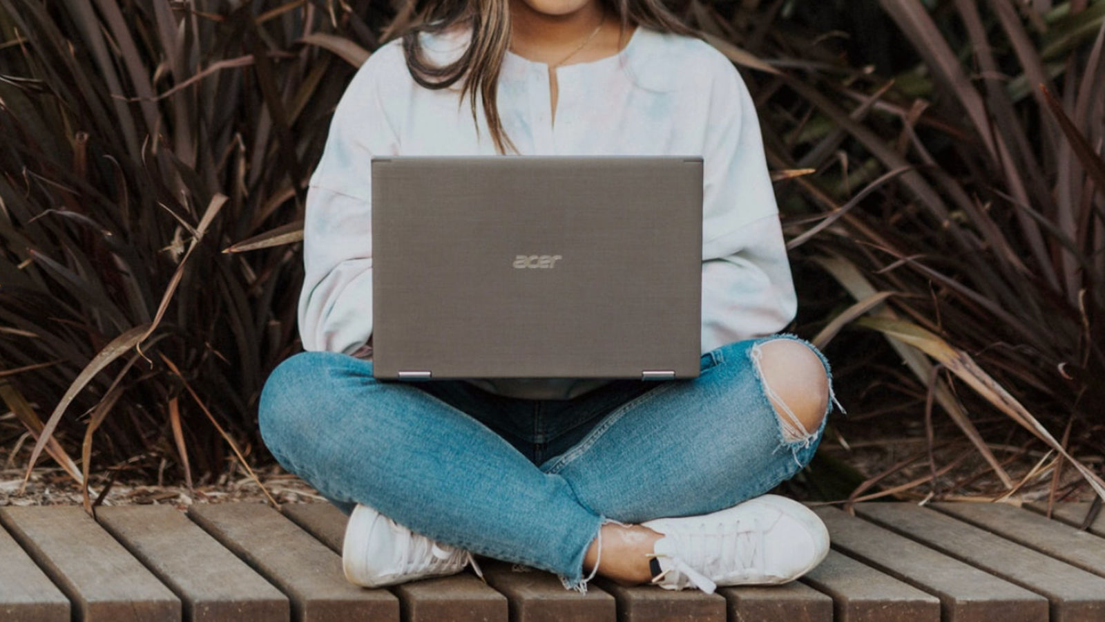 Girl typing on a computer outside by a plant