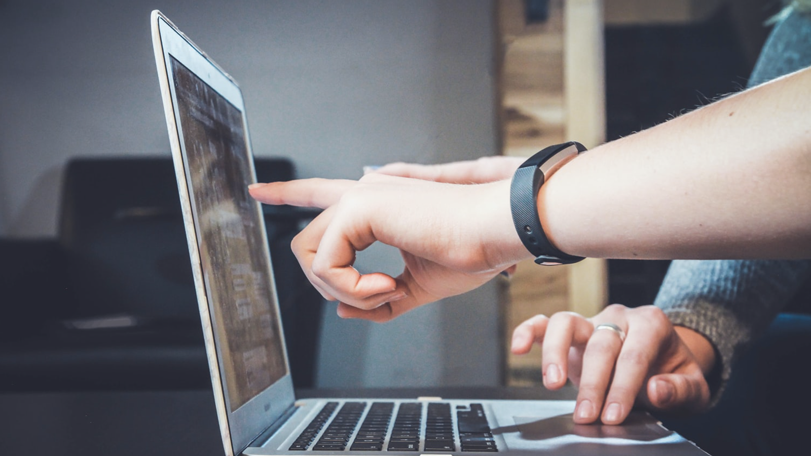 2 people working on a laptop; 1 is pointing on the screen, the other using the mousepad