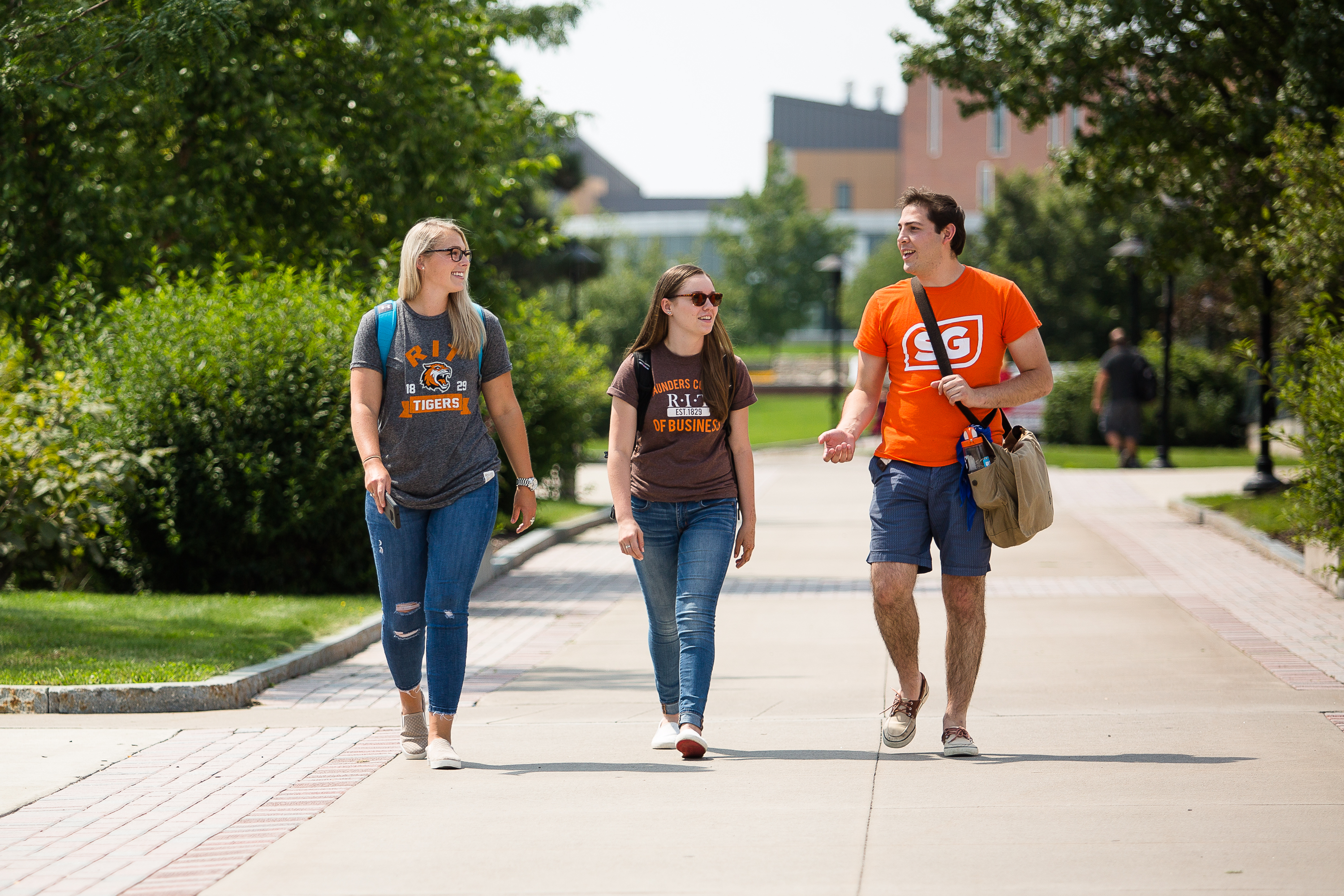 3 RIT students walking down a sidewalk next to the Saunders building