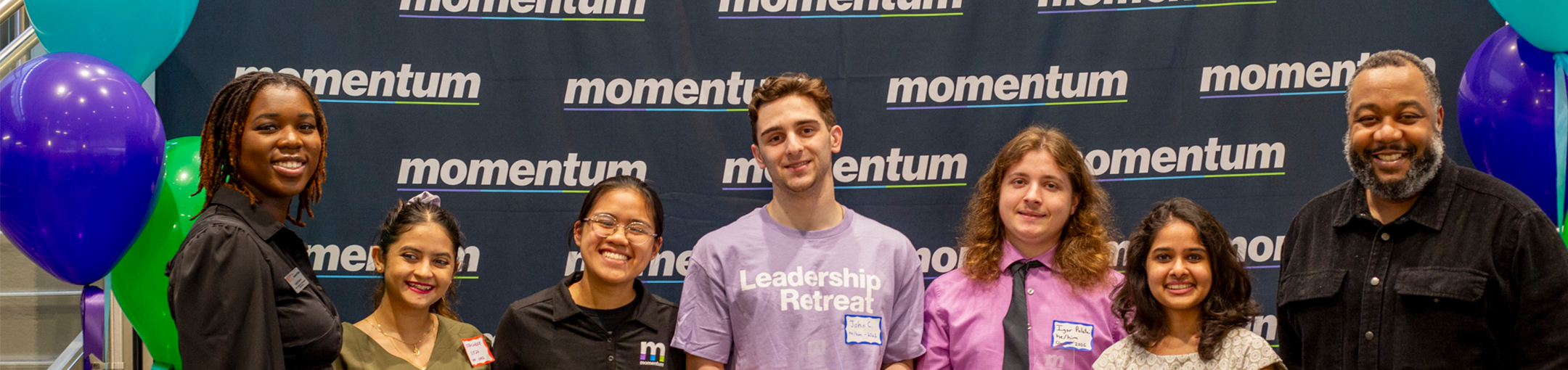 Students and staff pose for a photo in front of a Momentum backdrop