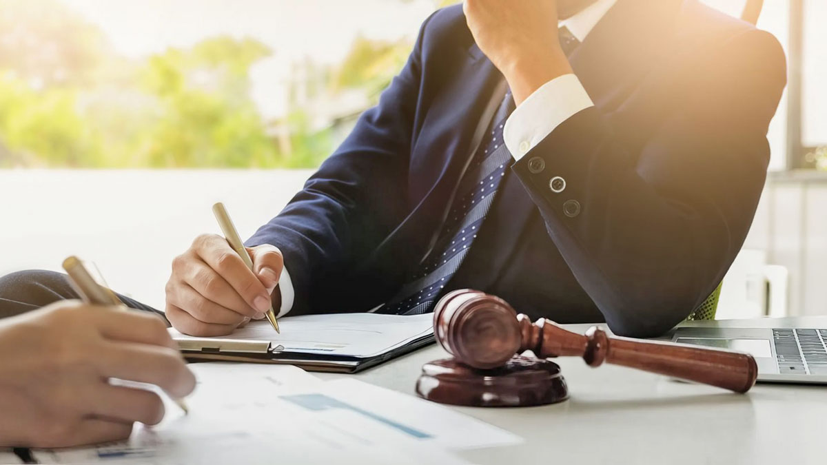 Close-up photo of two people sitting and writing at a table, which also has a gavel on it.