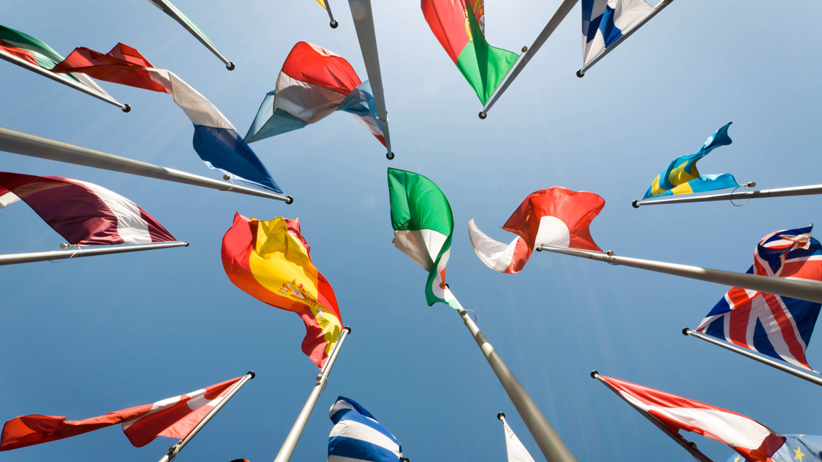 View from below of a variety of flags and blue sky.