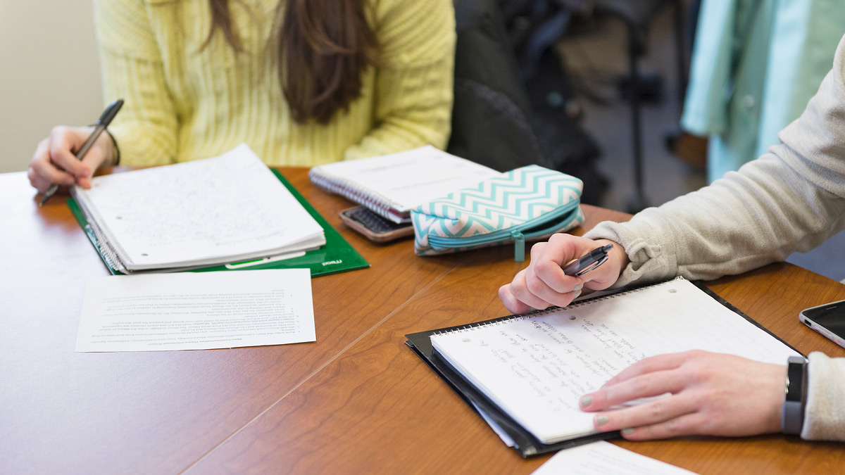 Close up of two students' hands with pens and notebooks.