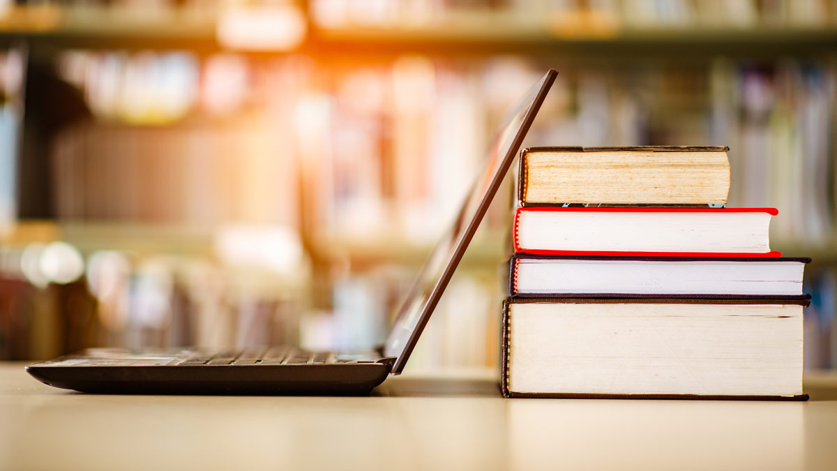 An open laptop computer monitor rests against a pile of books.