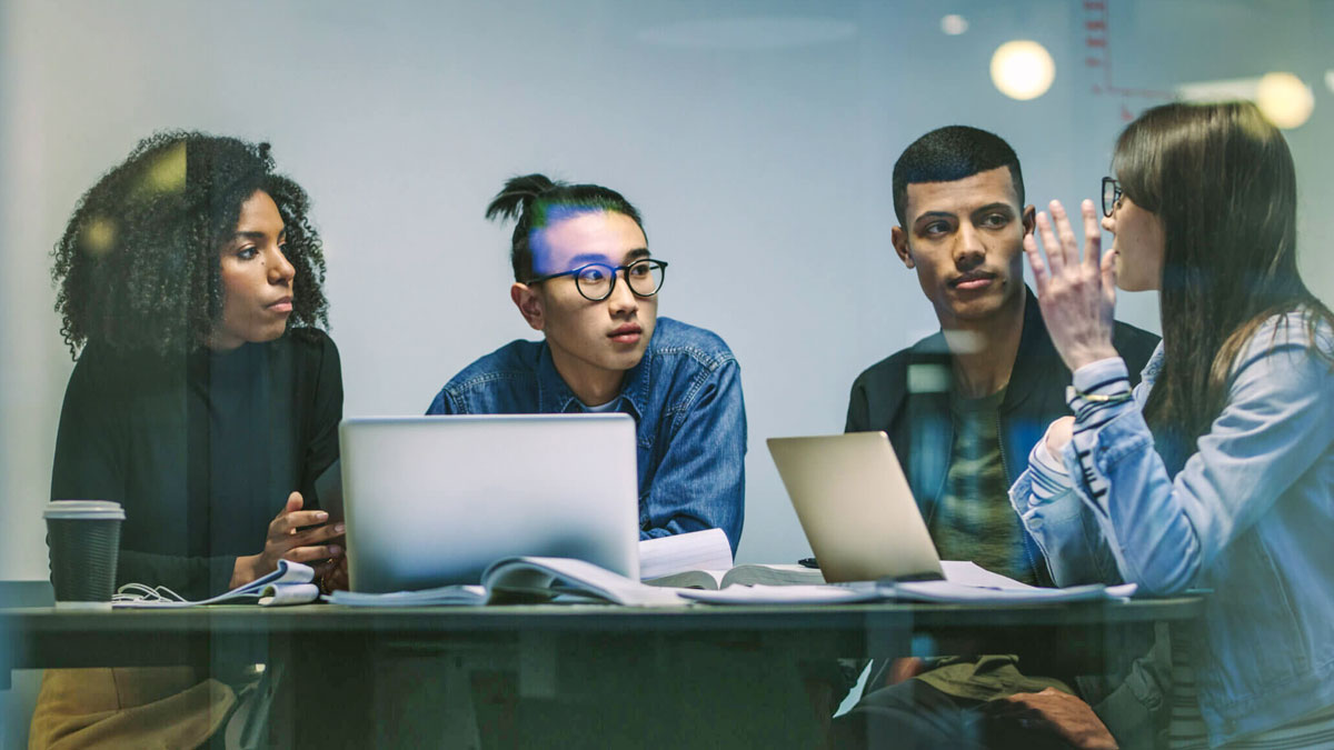 Four students talk while sitting in front of 2 laptops.