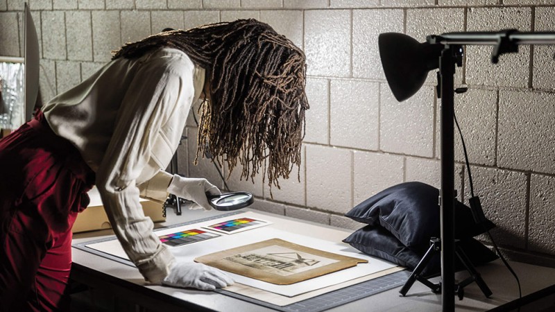 woman using a magnifying glass to look at a historic image on a table.