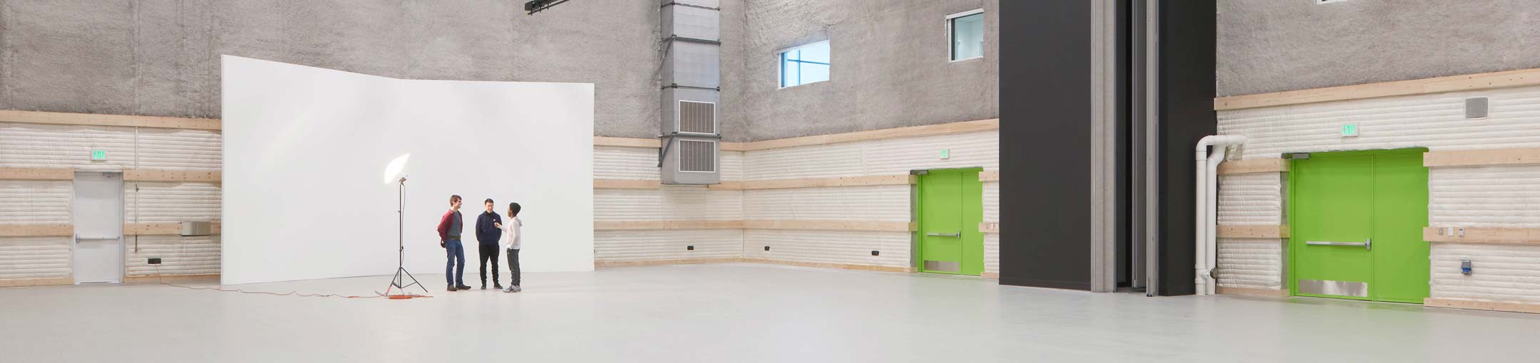 A large, open room with a white backdrop for photography with bright green doors